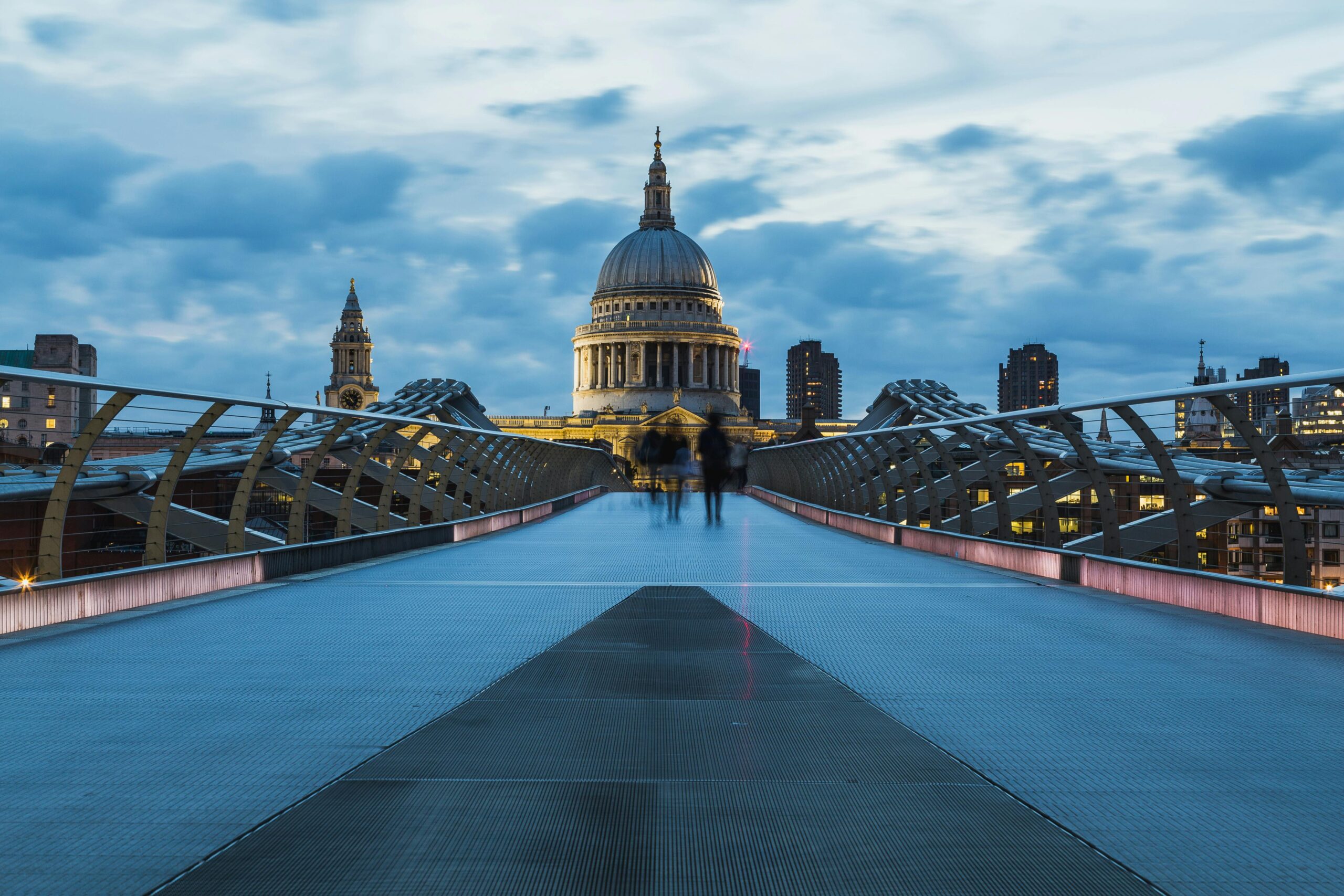 View of the Millennium Bridge leading to St Paul's Cathedral in London at dusk with a cloudy sky