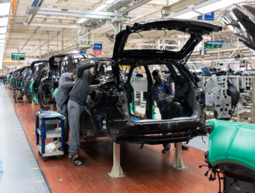 Workers on an assembly line collaboratively assembling cars, focused on their tasks in a busy manufacturing environment