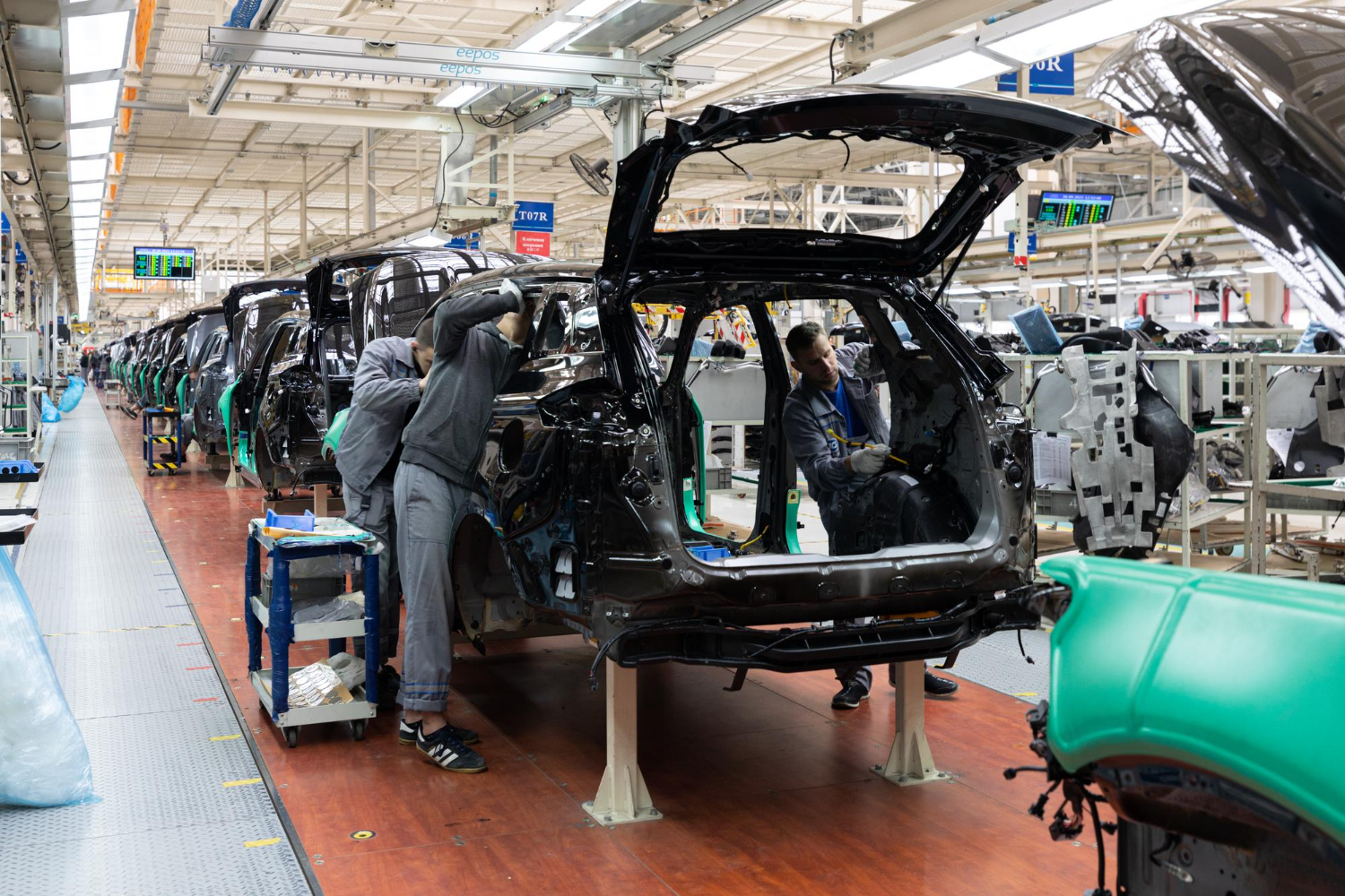 Workers on an assembly line collaboratively assembling cars, focused on their tasks in a busy manufacturing environment