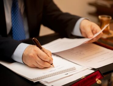 A man in a suit is focused on writing notes on a piece of paper at a desk