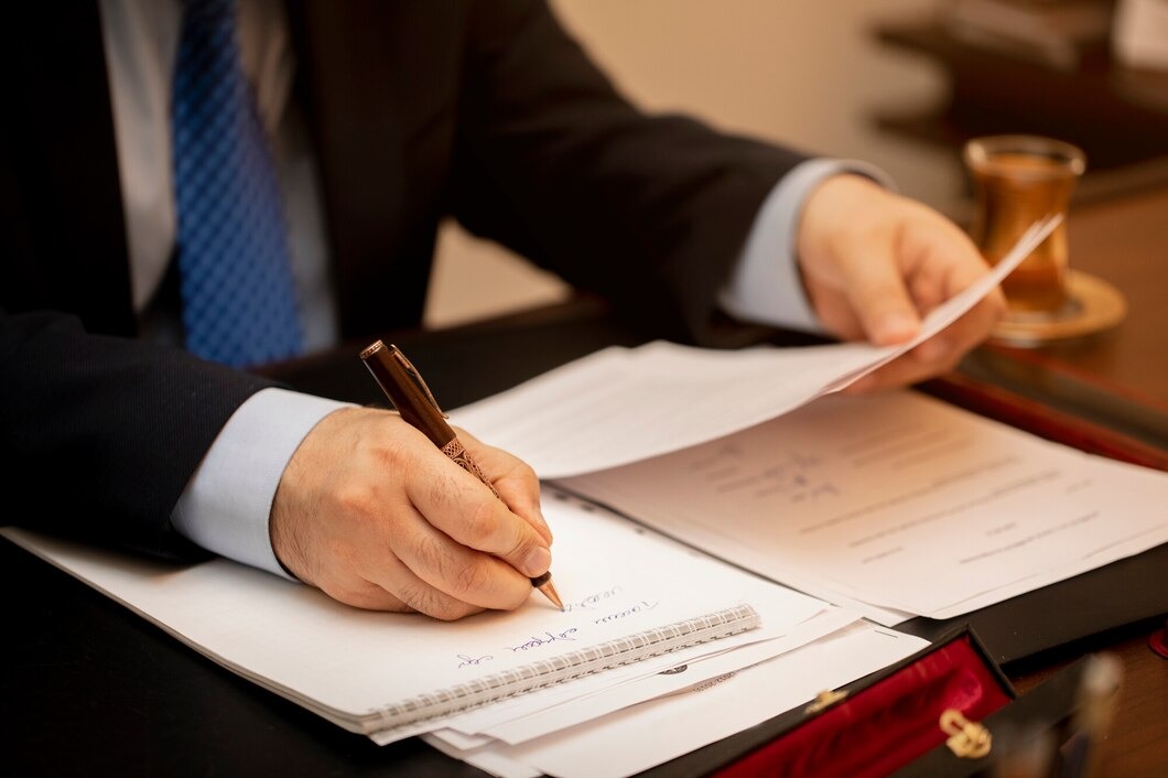 A man in a suit is focused on writing notes on a piece of paper at a desk